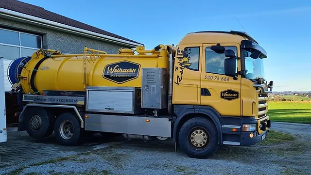 Gul tankbil parkert ved bygg og gresslette